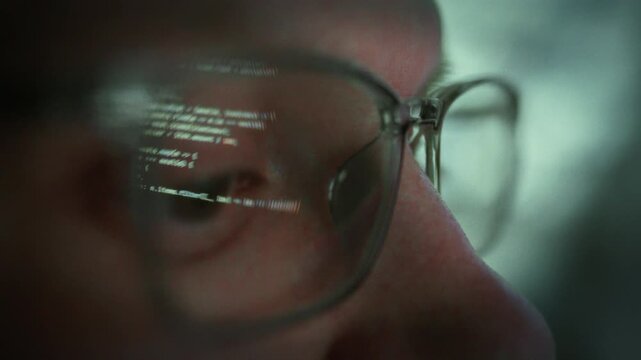 A programmer's eye, magnified in a close-up, focuses intently on lines of code while wearing glasses at night. The software engineer works diligently, writing complex code for a development project