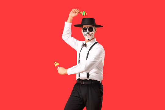 Young man with painted skull and maracas on red background. Mexico's Day of the Dead (El Dia de Muertos) celebration