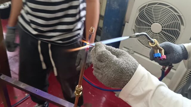 Technician welding AC pipe during air conditioner installation and repair. Close-up industrial maintenance work with metal pipe brazing for HVAC system service