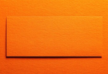 Fototapeta premium Orange card on textured orange surface with subtle shadow, top-down studio shot