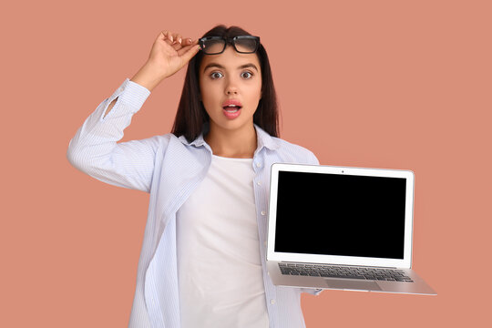 Shocked young female programmer with laptop on orange background