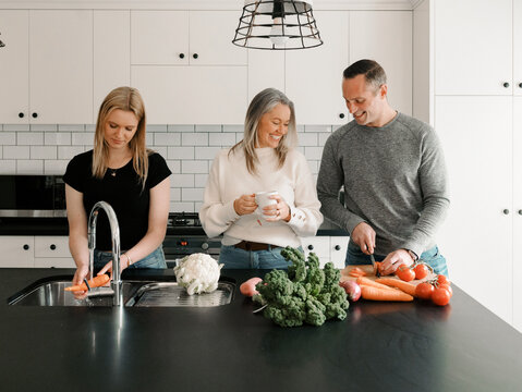 Teenage daughter helping dad prepare food by washing vegetables while mum stands holding a cup