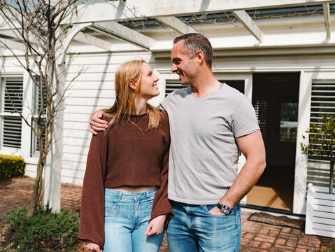 Father and teenage daughter stands closely looking at each other smiling in the patio on a sunny day