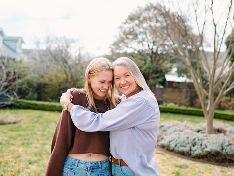 Mum hugging teenage daughter while standing in the backyard of their new home on a sunny day