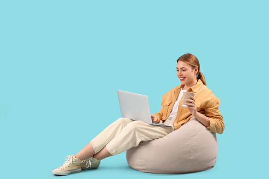 Female programmer with laptop and cup of coffee sitting on blue background