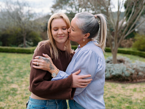 Mum hugging teenage daughter giving her a kiss on the cheek in the backyard