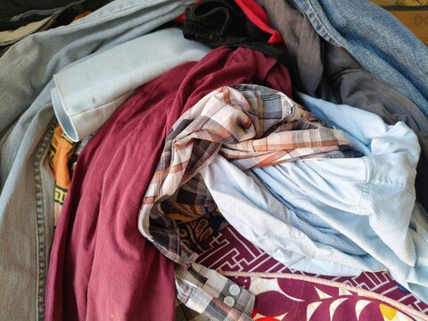 Overflowing clothes piled inside cramped cupboard shelves messy storage wardrobe cluttered fashion textile chaos home interior photography concept scene shot