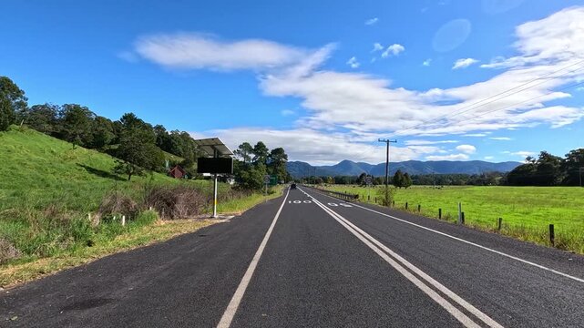 Driving on waterfall way, a scenic road trip with lush green paddocks and mountains under a clear blue sky.