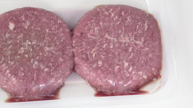Raw meat patties in plastic container presented close view for retail and food industry. Meat product shows fresh texture, meat distribution, packaging solutions and quality standards in supply chain
