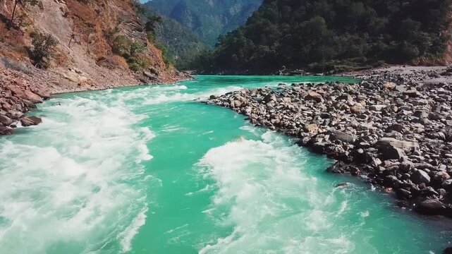 Turquoise rapids of the Ganga River flow between rocky banks in a forested mountain valley near Rishikesh, Uttarakhand. Smooth forward tracking shot follows the river upstream through the gorge.