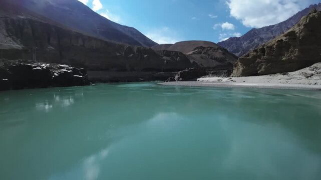 Turquoise glacial Indus river winds through barren high altitude Himalayan mountains of Ladakh region in India. FPV drone captures dynamic low-altitude flight along the rocky canyon wall and riverbank