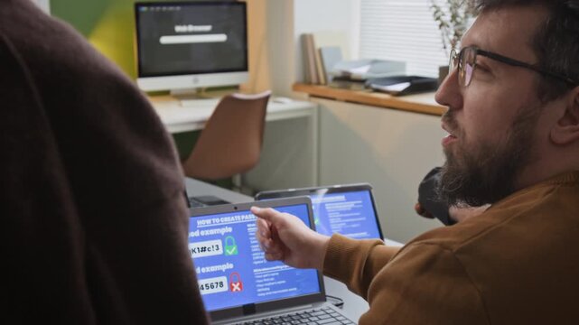 Zoom out shot of male teacher pointing to safe password practices shown on laptop screen while talking about digital safety to group of adults in computer literacy class, copy space