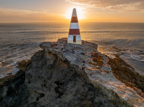Aerial view of a golden sunset behind a obelisk monument on a rocky coastal cliff top