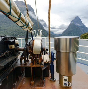 Front of a large yacht with a furled sail and equipment with mountains in the background