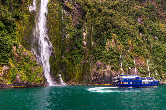 Large tour boat turning on green water near a waterfall