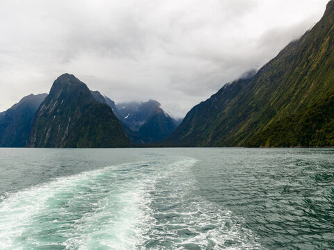 Wake of a boat on large body of water with mountains and cloudy sky