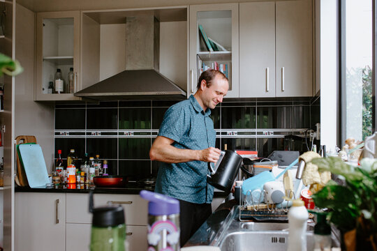 Caucasian man pouring hot water from electric kettle into the blue mug