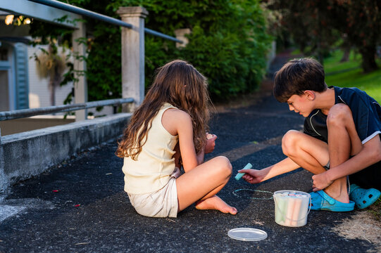 Two children siting on a path in New Zealand, drawing with chalk in the afternoon light