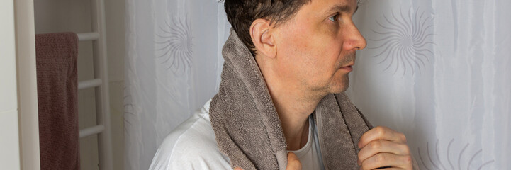 A 53-year-old man stands in the bathroom with a towel over his head while preparing for the day. He is focused on his morning tasks, surrounded by a clean setting, banner © pundapanda