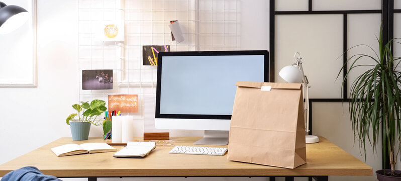 Workplace with computer and paper bag in office. Food delivery service
