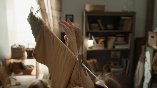 High angle shot of unrecognizable woman putting wrt clothes on clothesline while her son helping her inside their small poor apartment