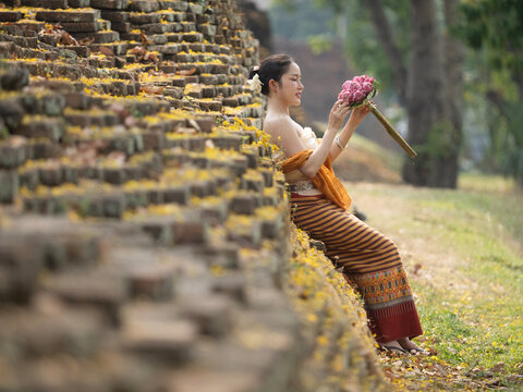 A beautiful young woman dressed in Lanna traditional walks the blooming yellow Ratchaphruek flowers in the old city of Chiang Mai.