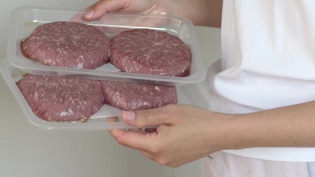 Hands holding package with raw beef patties in kitchen setting, retail and food concept for product marketing visuals. Beef highlights preparation and consumer choice.