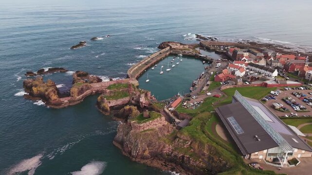 Cinematic aerial arc shot of a historic stone harbor and coastal bay, Scotland.