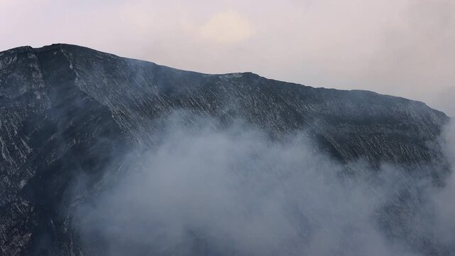 Dramatic mountain landscape shrouded in thick mist and volcanic smoke, with dark rocky ridges cutting through the clouds Mount Bromo in East Java, Indonesia