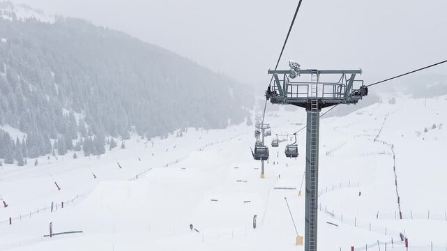 Ski lift rising above snowy slopes in Courchevel, France, surrounded by foggy alpine scenery during winter snowfall, with crowds of skiers descending the busy ski sl