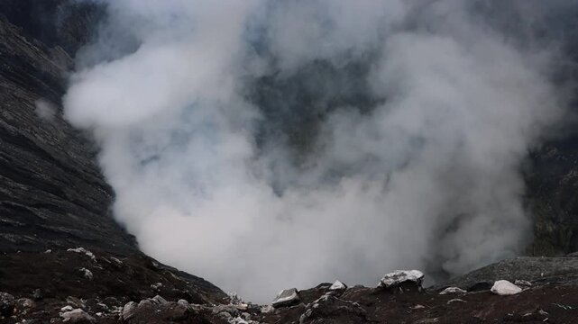 A dramatic aerial view of a volcanic crater with massive plumes of white steam rising from deep within the rugged landscape Mount Bromo in East Java, Indonesia
