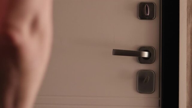 Close-up of a man's hand locking a door bolt and checking the handle. Process of securing a modern entrance door for home safety and privacy.