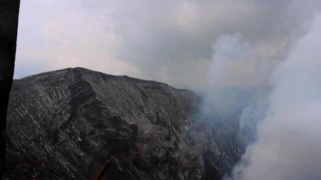 Dramatic mountain landscape shrouded in thick mist and volcanic smoke, with dark rocky ridges cutting through the clouds Mount Bromo in East Java, Indonesia