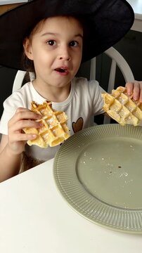 A beautiful young girl-child eats Belgian waffles with a happy face, smiles and laughs.