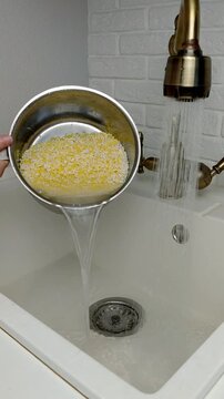 A woman rinses rice and millet in a pot under running water, close-up.