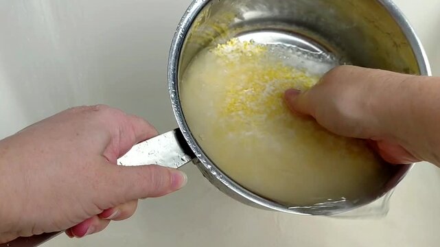 A woman rinses rice and millet in a pot under running water, close-up.