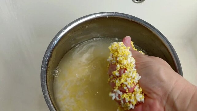 A woman rinses rice and millet in a pot under running water, close-up.