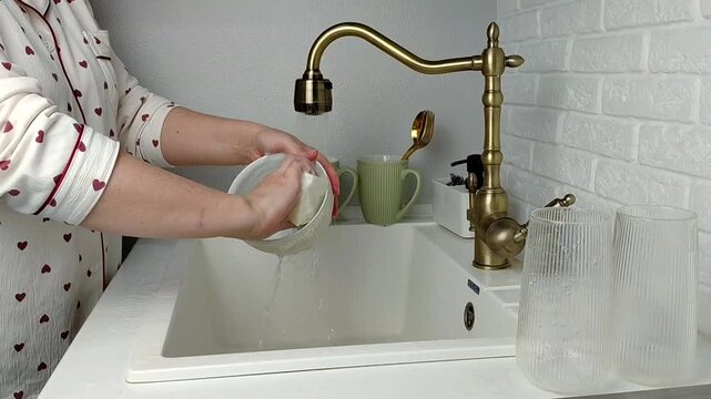 Woman washing dishes in kitchen sink, closeup. Cleaning chores
