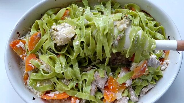 Green tagliatelle pasta is mixed with baked vegetables and turkey in a creamy sauce.