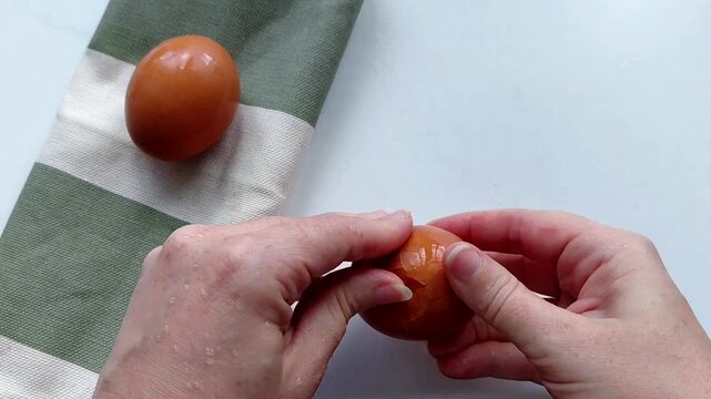 Removing egg shell, cleaning egg, health care concept. Close-up of hands peeling a boiled chicken egg, preparing ingredients for a homemade breakfast