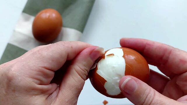 Removing egg shell, cleaning egg, health care concept. Close-up of hands peeling a boiled chicken egg, preparing ingredients for a homemade breakfast