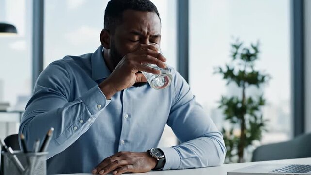 Serious Black Businessman Drinking Water in Office During Stressful Day at Work