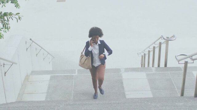 Businesswoman climbing outdoor stairs, speaking on phone after checking watch, quickening pace