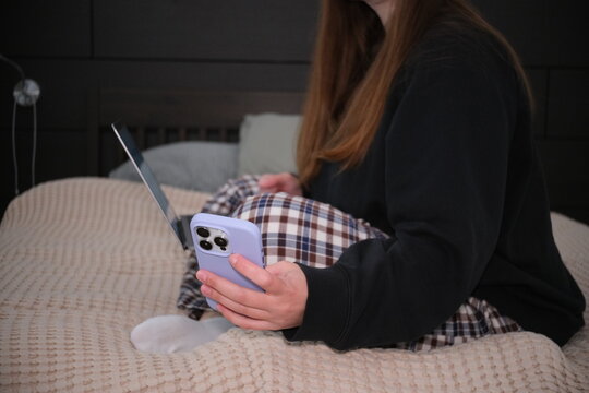 Woman using smartphone while sitting on bed in casual indoor lifestyle scene