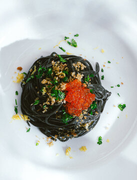 Black pasta with cuttlefish ink and red caviar, served with breadcrumbs fried in olive oil. Volcanic inspiration, seafood paste, black background, minimalist composition. Pasta with seafood