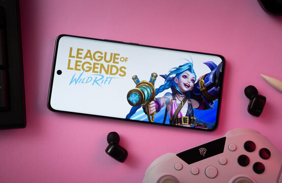 Dhaka, Bangladesh- 23 March 2025: Smartphone displaying League of Legends game on pink surface with earphones and controller nearby.