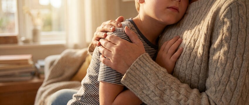 child adult support hug family comfort care trust closeup with caregiver arms wrapped around sad child on sofa suggesting protection reassurance secure attachment and gentle emotional healing