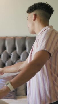Vertical video: Seeing box, man in striped shirt moving items, sitting on bed and adjusting pillow