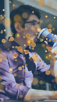 Vertical video: Man shifting and reaching cup pausing office sipping under gold hexagon overlay