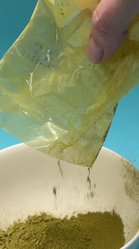 Female hands pour henna and indigo basma powder into white bowl for hair dye preparation closeup